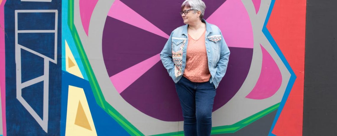Fiona Scott from Scott Media, standing in front of a bright abstract mural painted wall