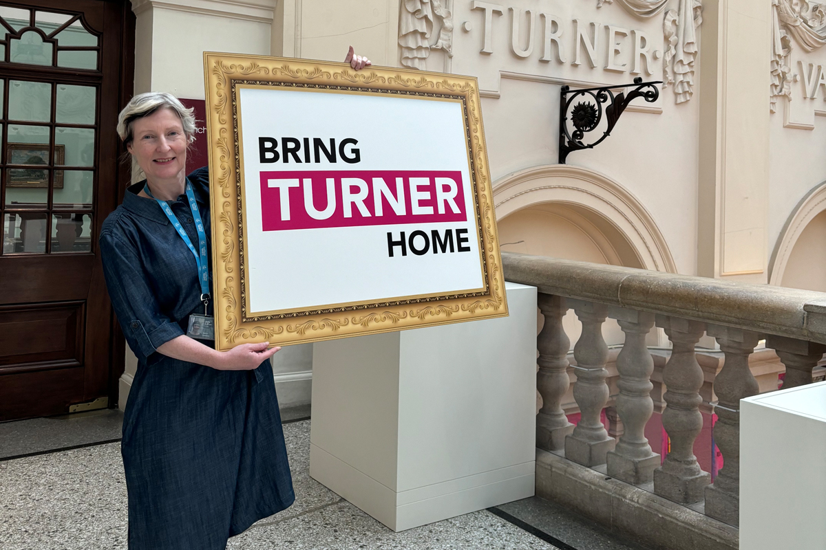 Julia Carver Curator, Visual Arts with Bring Turner Home sign in Bristol Museum – credit Strike Communications